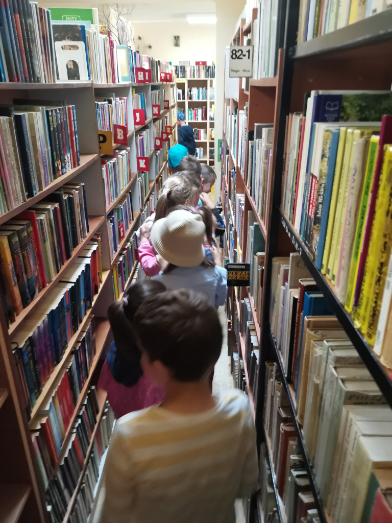 Zdjęcie przedstawia grupę dzieci zwiedzających bibliotekę bawiąc się w zabawę Wesoły pociąg